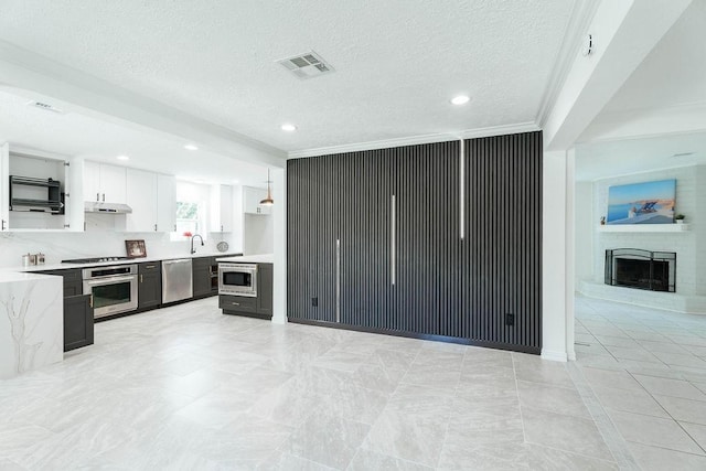 28926 Twisted Oak Dr, Shenandoah, TX 77381 - kitchen featuring stainless steel appliances, light countertops, under cabinet range hood, open floor plan, and white cabinets