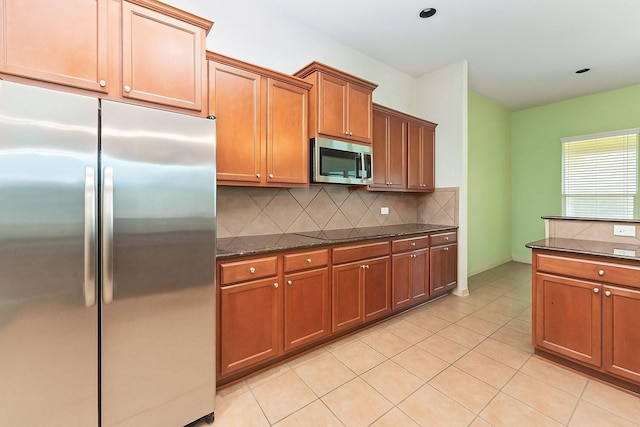 18843 Cove Pointe Dr, Cypress, TX 77433 - kitchen featuring stainless steel appliances, tasteful backsplash, brown cabinets, dark stone counters, and light tile patterned flooring