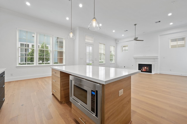 614 Delmar St, Houston, TX 77023 - kitchen featuring stainless steel microwave, a warm lit fireplace, modern cabinets, light wood finished floors, and recessed lighting