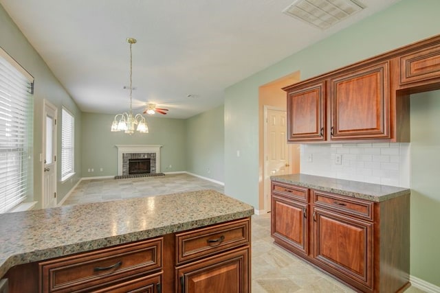 2917 Veva Dr, Pearland, TX 77584 - kitchen with backsplash, light stone counters, a brick fireplace, pendant lighting, and a chandelier