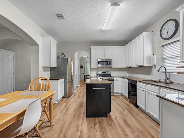 13923 Roanoke Falls Dr, Cypress, TX 77429 - kitchen featuring appliances with stainless steel finishes, arched walkways, a kitchen island, light wood-type flooring, and white cabinetry