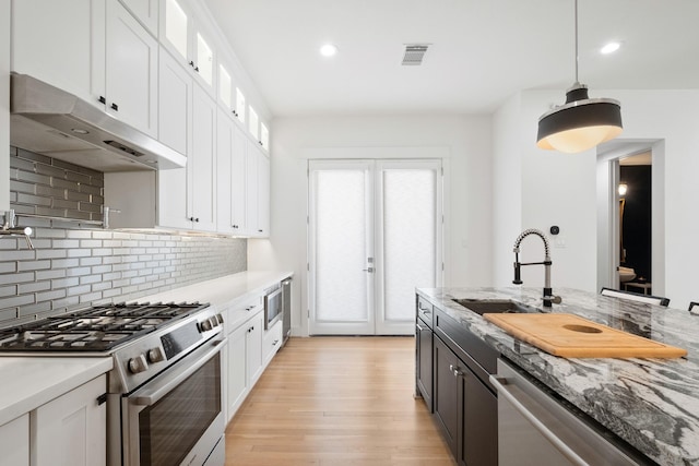 1405 Indiana St Unit B, Houston, TX 77006 - kitchen featuring appliances with stainless steel finishes, under cabinet range hood, light wood finished floors, white cabinets, and decorative backsplash