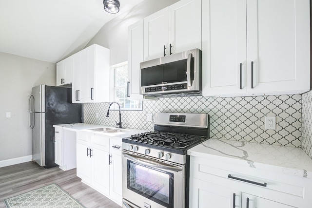 1111 Robinson St, Alvin, TX 77511 - kitchen with stainless steel appliances, vaulted ceiling, white cabinetry, light stone counters, and backsplash