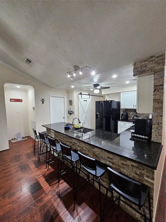 19423 Quiet Brook Dr, Houston, TX 77084 - kitchen with black fridge with ice dispenser, a barn door, dark wood-style flooring, a textured ceiling, and a breakfast bar area