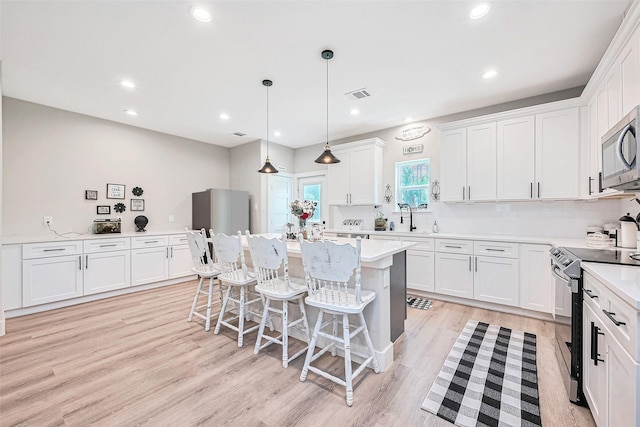 807 Ave J Pl, Conroe, TX 77301 - kitchen with stainless steel appliances, white cabinets, a kitchen breakfast bar, light wood-style floors, and recessed lighting