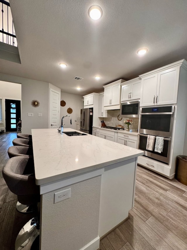 15814 Weston Ridge Dr, Humble, TX 77346 - kitchen featuring light wood-style flooring, white cabinetry, appliances with stainless steel finishes, an island with sink, and a textured ceiling