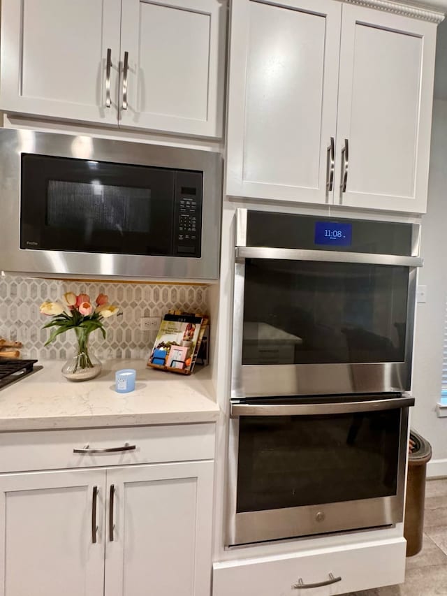 15814 Weston Ridge Dr, Humble, TX 77346 - kitchen with double oven, built in microwave, tasteful backsplash, white cabinetry, and light stone counters