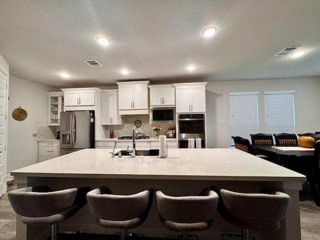 15814 Weston Ridge Dr, Humble, TX 77346 - kitchen with decorative backsplash, appliances with stainless steel finishes, white cabinets, a large island with sink, and recessed lighting