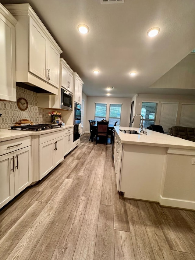 15814 Weston Ridge Dr, Humble, TX 77346 - kitchen with light wood-style flooring, light countertops, white cabinets, tasteful backsplash, and recessed lighting
