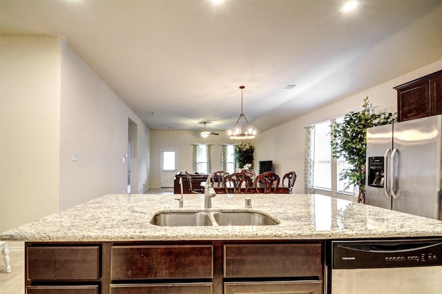 12223 Antilles Ln, Conroe, TX 77304 - kitchen featuring stainless steel appliances, dark brown cabinets, a chandelier, an island with sink, and light stone counters