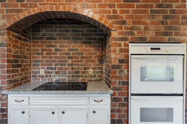 27093 Frye Rd, Splendora, TX 77372 - kitchen with double oven, white cabinetry, light stone countertops, brick wall, and black electric stovetop