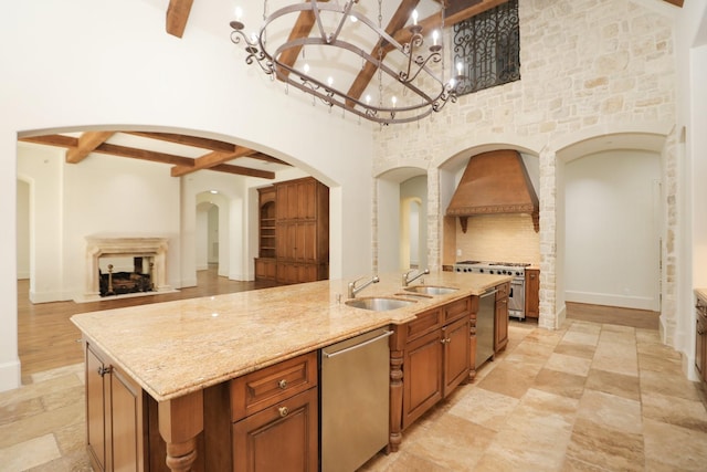 764 Kuhlman Rd, Hunters Creek Village, TX 77024 - kitchen with beamed ceiling, appliances with stainless steel finishes, brown cabinetry, an island with sink, and light stone counters
