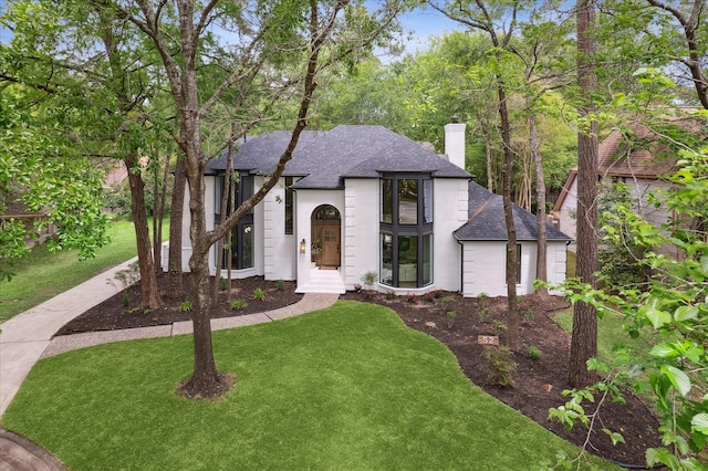 52 Indian Clover, The Woodlands, TX 77381 - french country home with roof with shingles, a chimney, a front lawn, and brick siding
