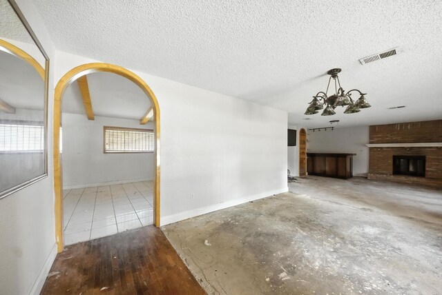 3819 Galway Ln, Houston, TX 77080 - unfurnished living room featuring a chandelier, a textured ceiling, a brick fireplace, and arched walkways