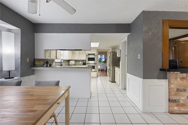 727 Baltic Ln, Houston, TX 77090 - kitchen featuring ceiling fan, a peninsula, appliances with stainless steel finishes, light tile patterned flooring, and a textured ceiling