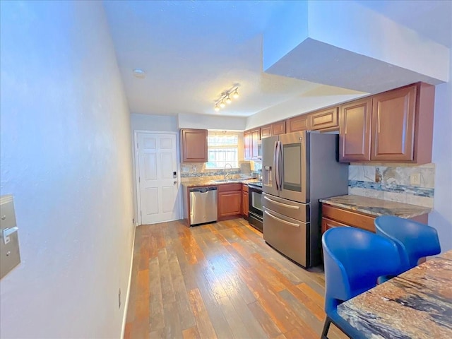 6305 Westward St Unit 106, Houston, TX 77081 - kitchen featuring stainless steel appliances, light wood-style floors, backsplash, and brown cabinets