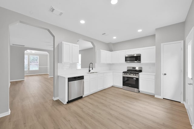 23911 Pinecreek Pt, Spring, TX 77373 - kitchen featuring arched walkways, stainless steel appliances, light wood finished floors, white cabinetry, and recessed lighting