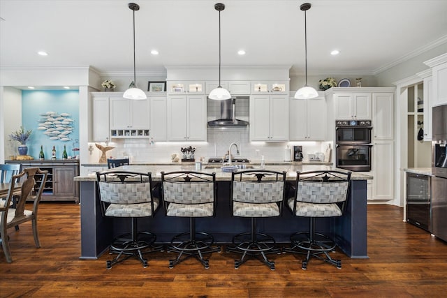 3848 S Main St, Anahuac, TX 77514 - kitchen with a center island with sink, wall chimney exhaust hood, a kitchen breakfast bar, white cabinets, and ornamental molding