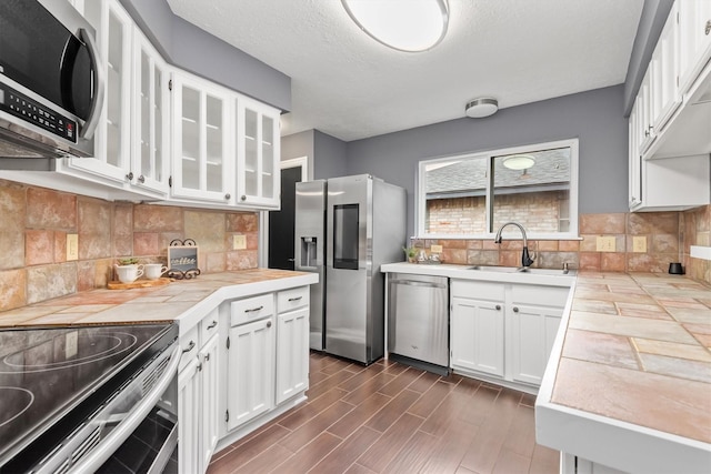 6510 Barrygate Dr, Spring, TX 77373 - kitchen with appliances with stainless steel finishes, white cabinetry, tile countertops, glass insert cabinets, and tasteful backsplash