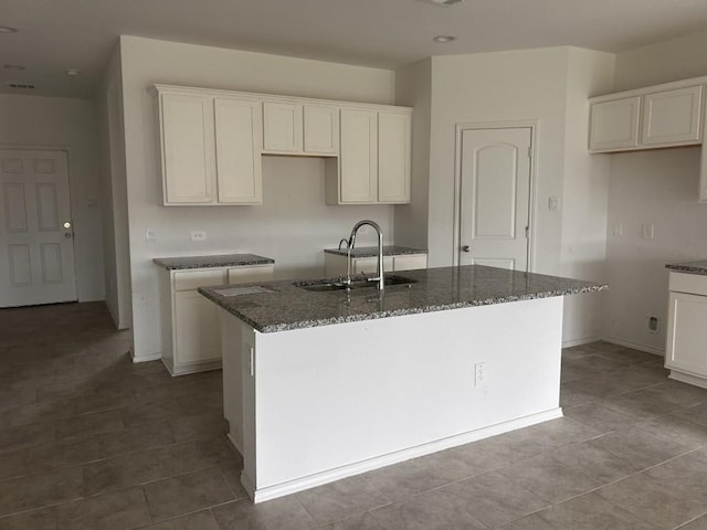 14217 Dream Rd, New Caney, TX 77357 - kitchen with an island with sink, dark stone counters, tile patterned flooring, and white cabinetry