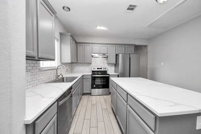 9805 Kerr, Houston, TX 77029 - kitchen featuring gray cabinetry, stainless steel appliances, a kitchen island, decorative backsplash, and under cabinet range hood