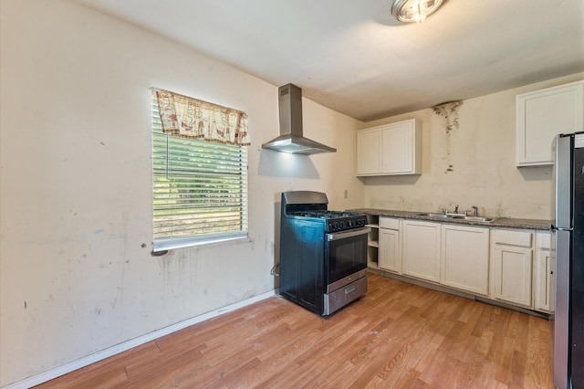 8121 Woodlyn Rd, Houston, TX 77028 - kitchen with stainless steel appliances, light wood finished floors, white cabinets, wall chimney range hood, and dark countertops