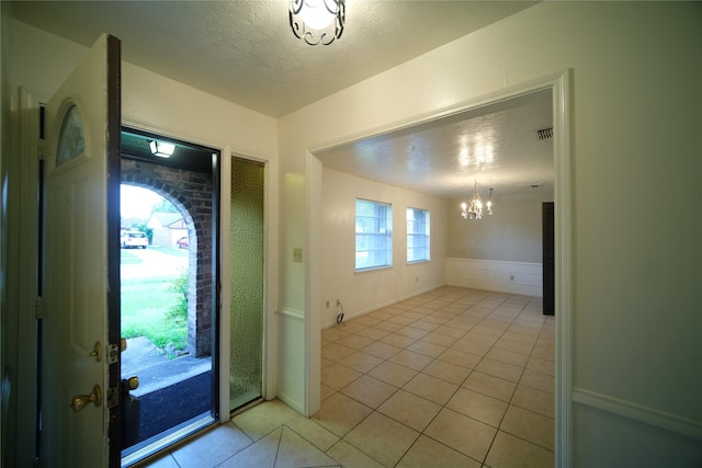 entrance foyer featuring an inviting chandelier, a textured ceiling, and light tile floors