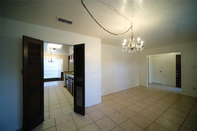 tiled empty room featuring a notable chandelier and a textured ceiling