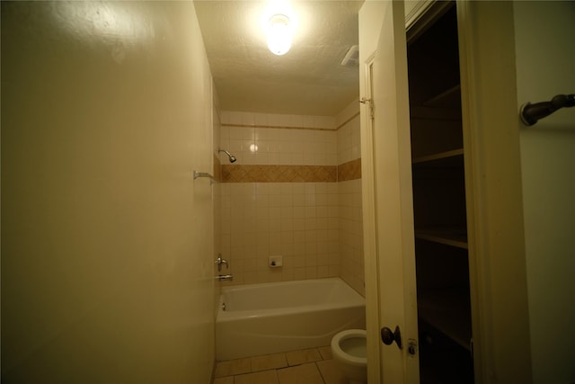 bathroom with a textured ceiling, tile floors, toilet, and tiled shower / bath