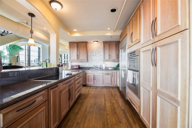 kitchen featuring decorative light fixtures, dark wood-type flooring, backsplash, a tray ceiling, and dark stone countertops