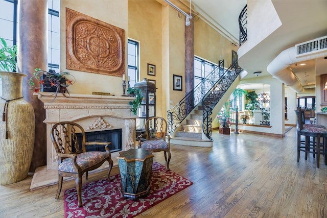 sitting room featuring a towering ceiling, a notable chandelier, a premium fireplace, and wood-type flooring