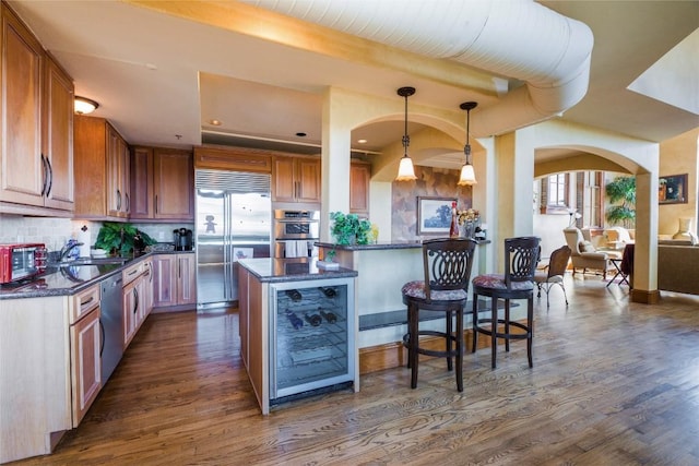 kitchen featuring appliances with stainless steel finishes, hanging light fixtures, dark wood-type flooring, a kitchen island, and backsplash