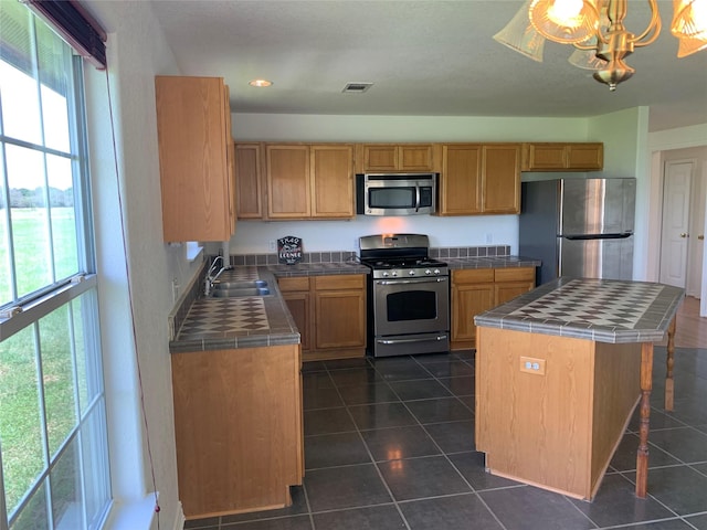 kitchen featuring a kitchen island, tile counters, stainless steel appliances, a notable chandelier, and sink