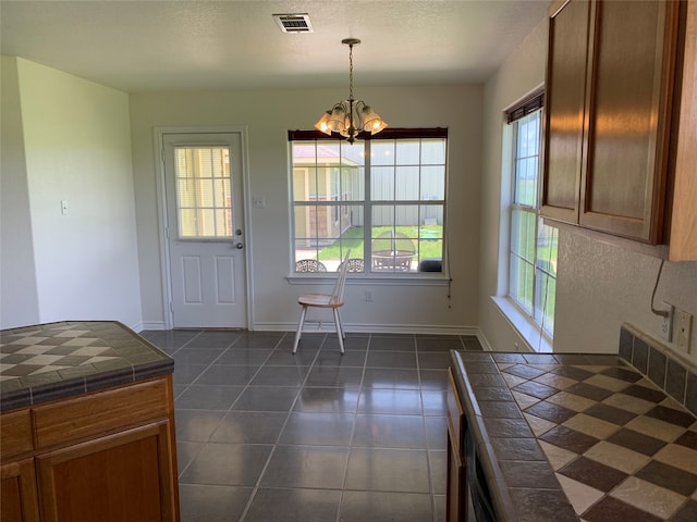 kitchen featuring dark tile floors, a notable chandelier, tile countertops, and pendant lighting