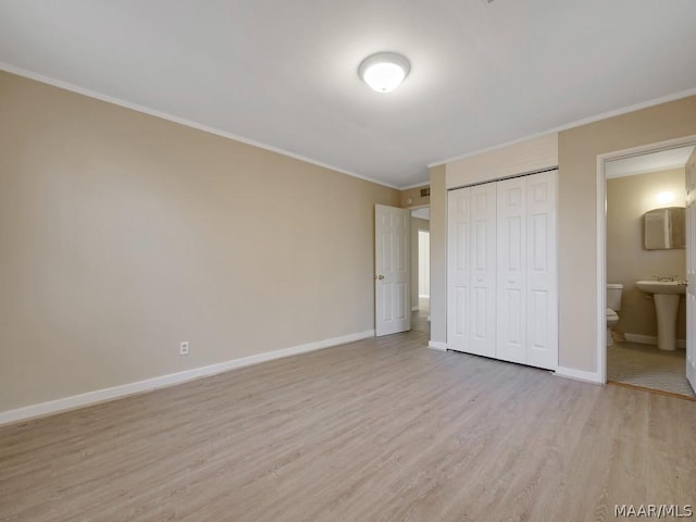 unfurnished bedroom featuring ensuite bathroom, a closet, light hardwood / wood-style flooring, and crown molding