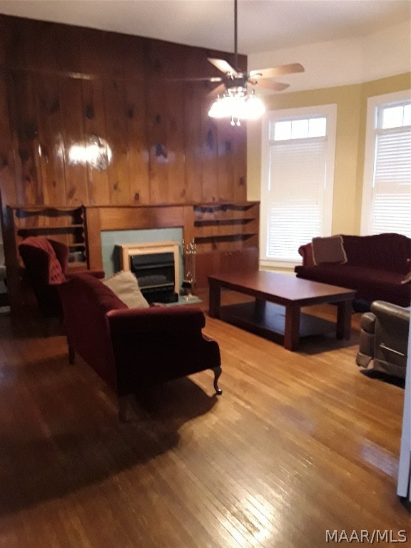 living room with ceiling fan, light wood-type flooring, and wood walls