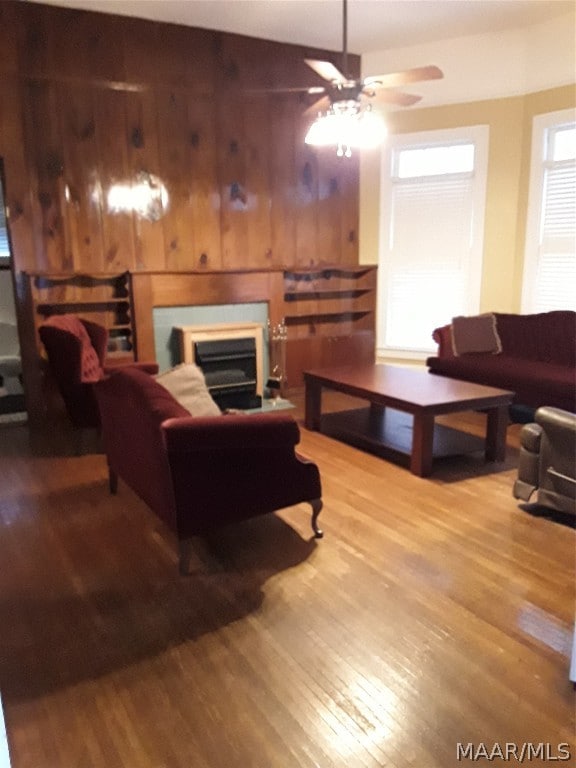 living room featuring ceiling fan, light wood-type flooring, and wood walls