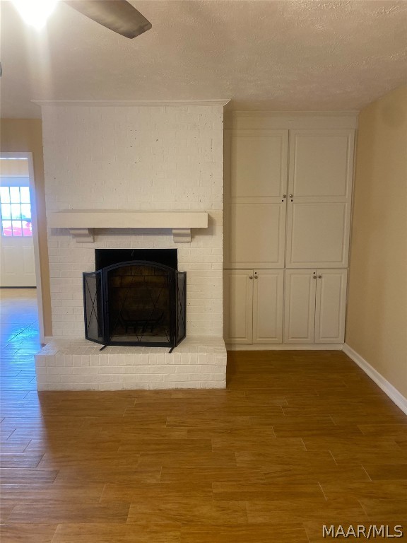 unfurnished living room with light wood-type flooring, a textured ceiling, ceiling fan, and a fireplace