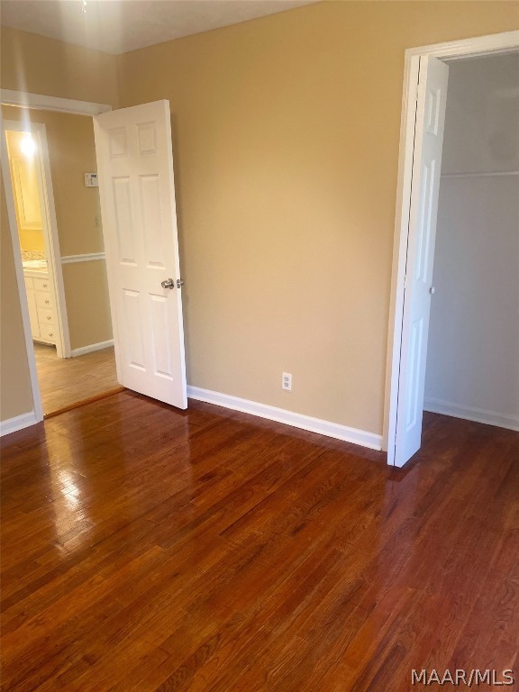 unfurnished bedroom with ensuite bathroom and dark hardwood / wood-style flooring