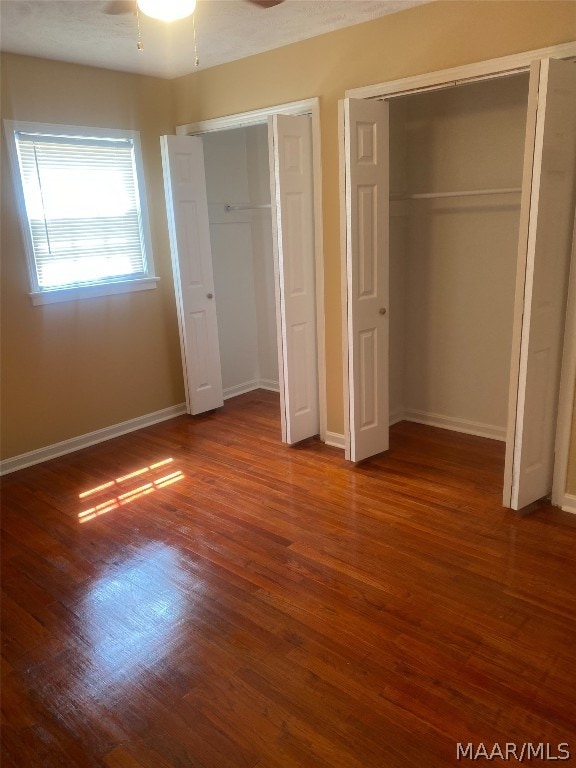 unfurnished bedroom featuring multiple closets, ceiling fan, and dark wood-type flooring