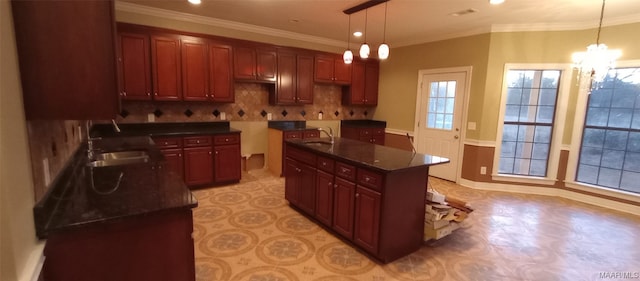 kitchen with hanging light fixtures, backsplash, a notable chandelier, sink, and an island with sink