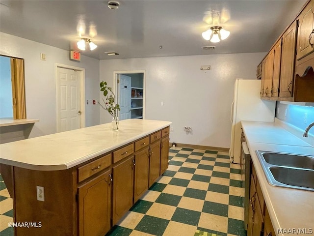 kitchen with dishwashing machine, a kitchen island, light tile floors, and sink