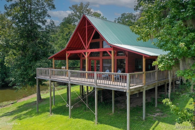 rear view of property featuring a deck with water view and a lawn