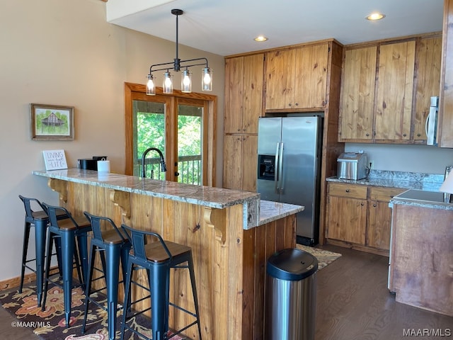 kitchen with dark wood-type flooring, a kitchen bar, light stone counters, stainless steel refrigerator with ice dispenser, and pendant lighting