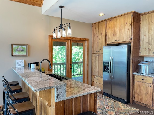 kitchen with stainless steel fridge, sink, hanging light fixtures, a breakfast bar area, and light stone countertops