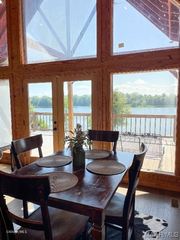 dining space featuring french doors, a water view, hardwood / wood-style flooring, and a towering ceiling