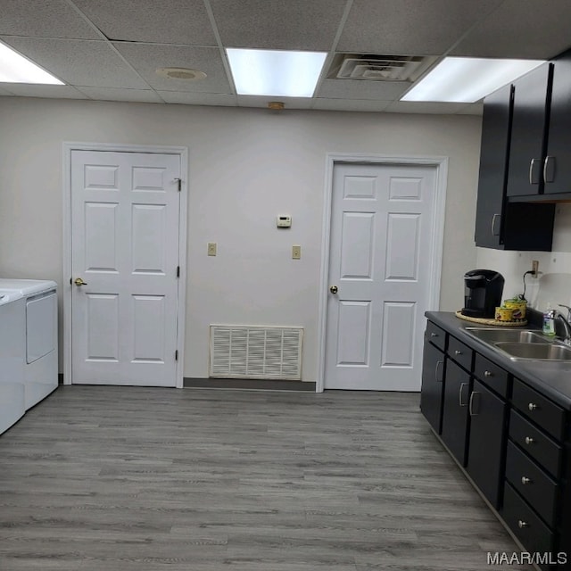 kitchen with a paneled ceiling, light hardwood / wood-style flooring, washing machine and clothes dryer, and sink