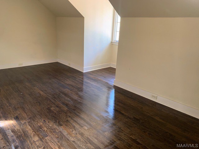 spare room featuring dark wood-type flooring and vaulted ceiling