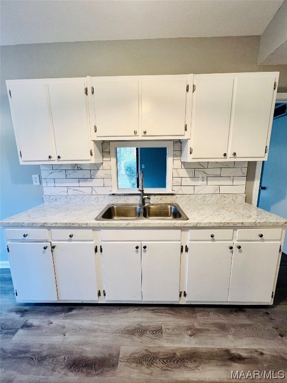 kitchen featuring sink, light stone counters, white cabinets, wood-type flooring, and tasteful backsplash