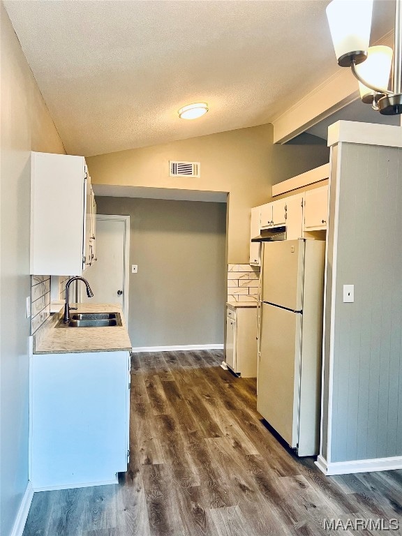 kitchen featuring white cabinetry, backsplash, white fridge, sink, and vaulted ceiling